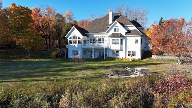 back of property with a lawn, a chimney, a balcony, and a shingled roof