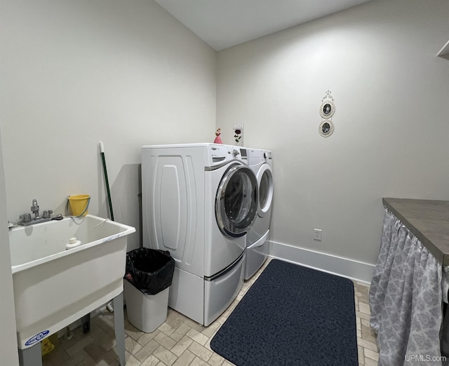 clothes washing area featuring baseboards, washer and clothes dryer, laundry area, and a sink