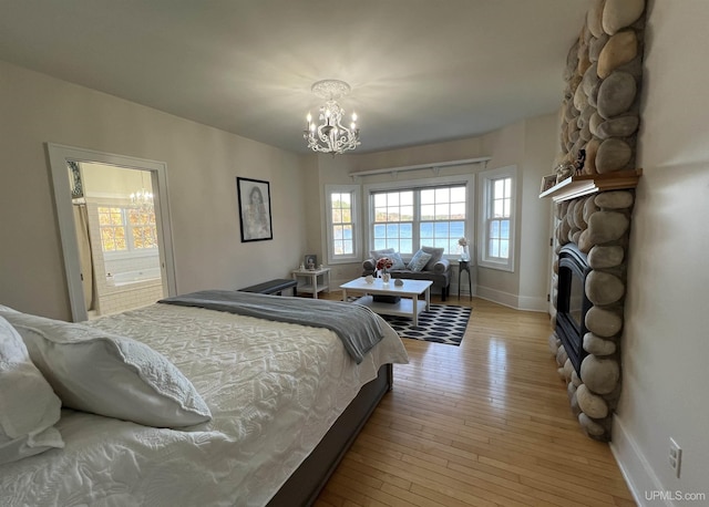 bedroom with baseboards, light wood-style flooring, a stone fireplace, and an inviting chandelier