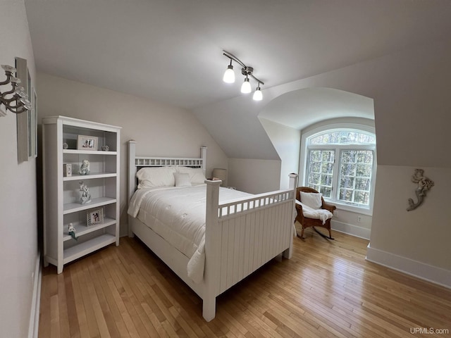 bedroom with light wood-style floors, lofted ceiling, and baseboards