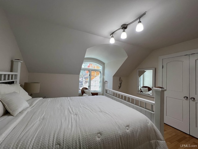 bedroom with a closet, vaulted ceiling, rail lighting, and light wood finished floors