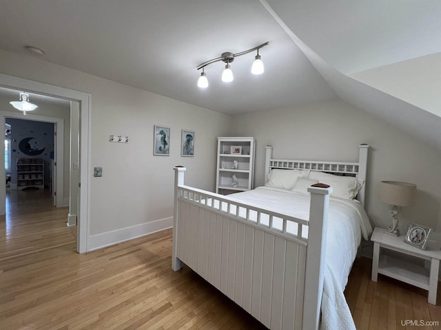 bedroom featuring baseboards, vaulted ceiling, and light wood-type flooring