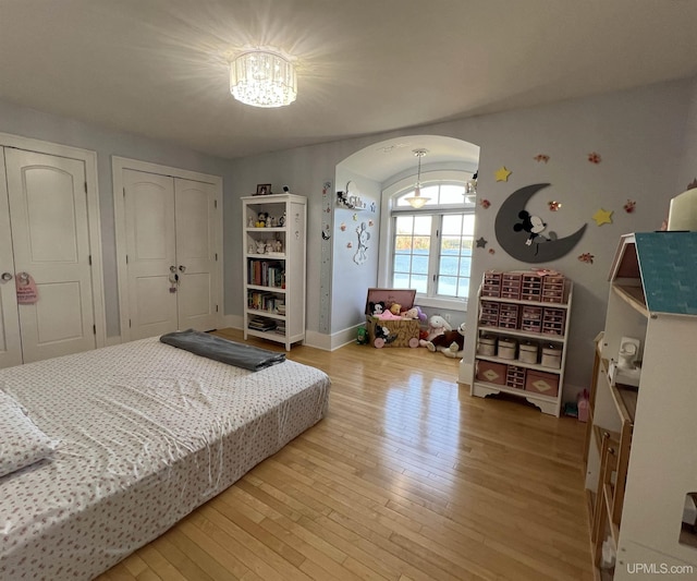 bedroom with baseboards, arched walkways, light wood-style floors, and two closets