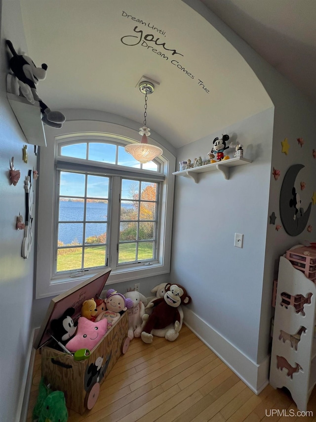 rec room with wood-type flooring, a water view, and vaulted ceiling