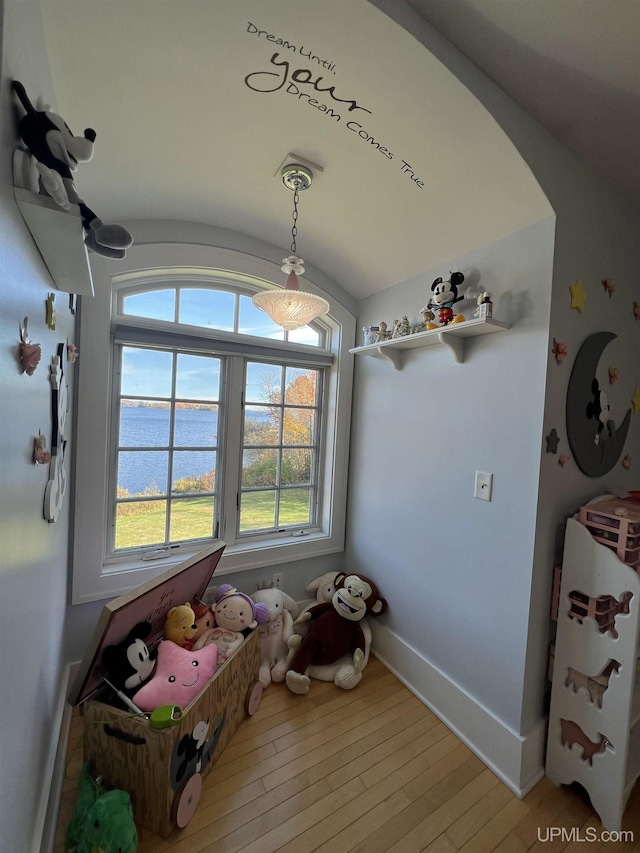 interior space with light wood-type flooring, a water view, lofted ceiling, and baseboards