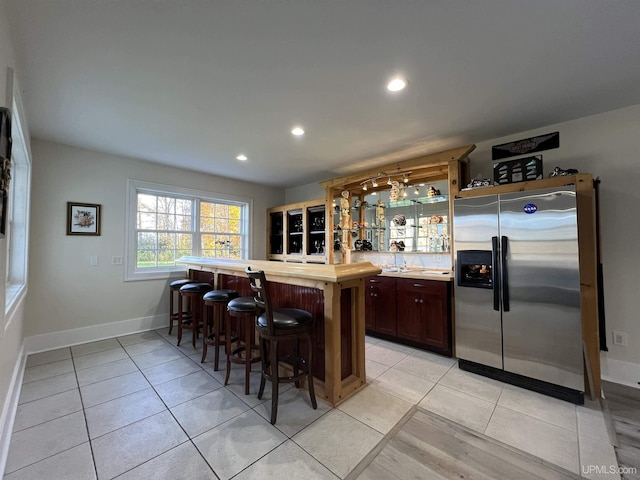 kitchen with a breakfast bar, light tile patterned floors, stainless steel fridge, light countertops, and recessed lighting