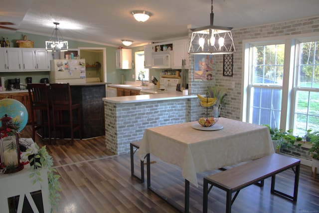 dining room with brick wall, vaulted ceiling, an inviting chandelier, and dark hardwood / wood-style flooring