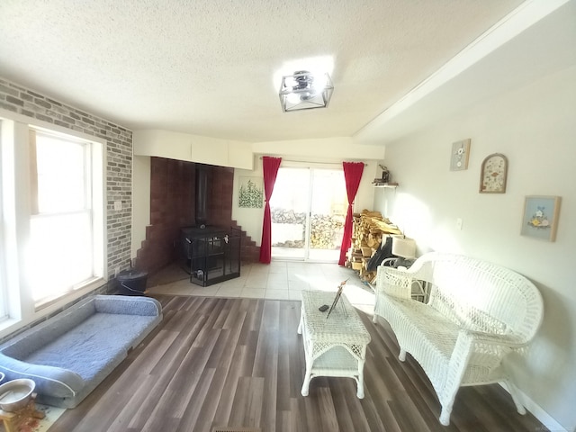 living area with brick wall, hardwood / wood-style floors, a textured ceiling, and a wood stove