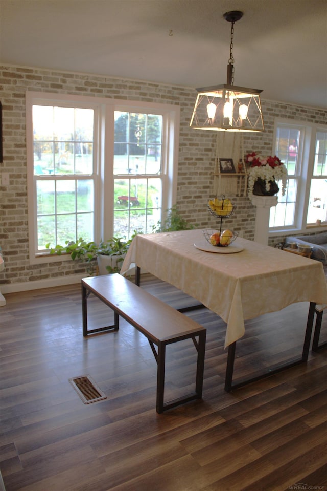 dining room featuring a notable chandelier, brick wall, and dark hardwood / wood-style flooring