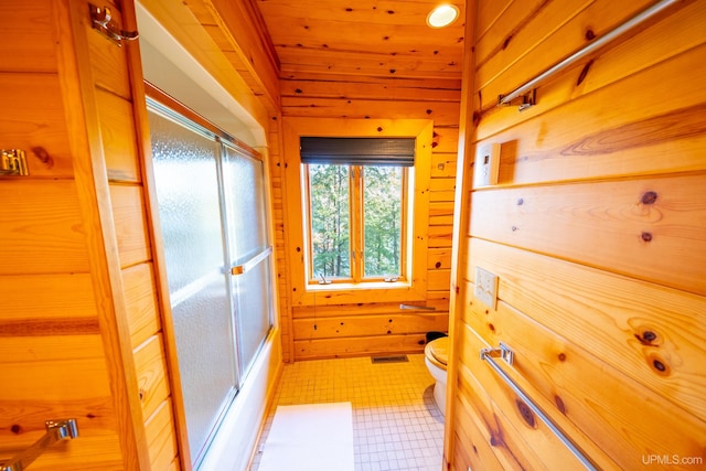 bathroom featuring toilet, wood ceiling, bath / shower combo with glass door, and wooden walls