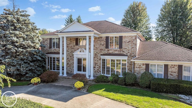 neoclassical home featuring brick siding, a front yard, and roof with shingles