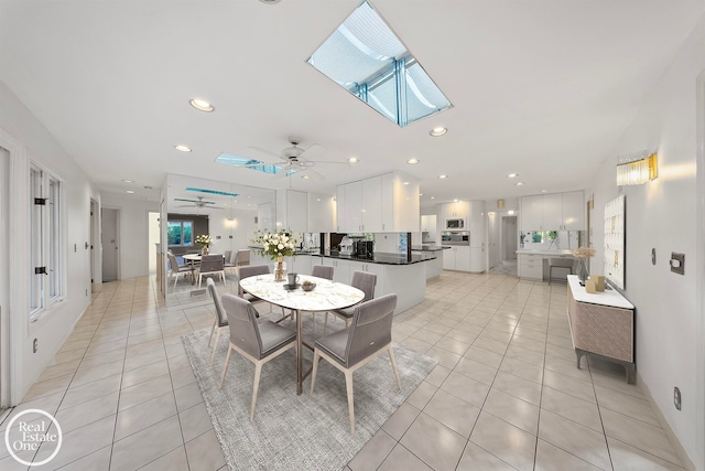 tiled dining room featuring ceiling fan and a skylight