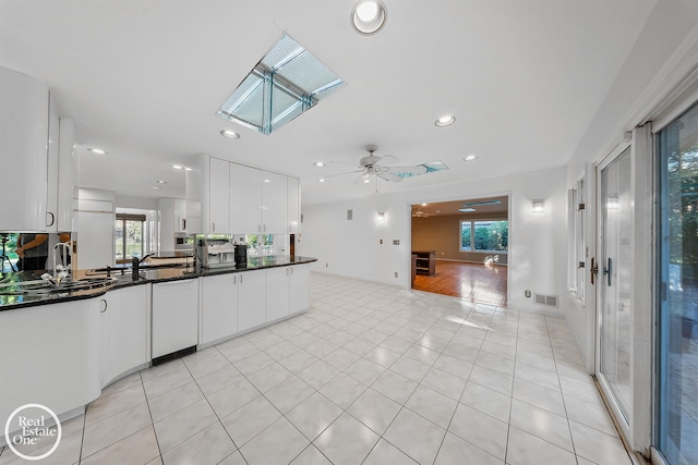 kitchen with ceiling fan, a skylight, light tile patterned floors, and white cabinets