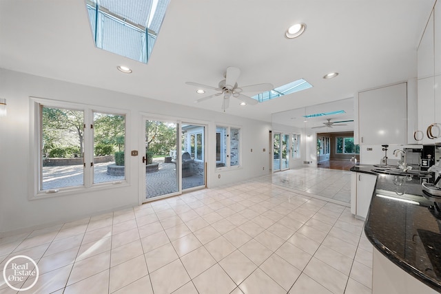 unfurnished living room featuring sink, light tile patterned flooring, ceiling fan, and a skylight