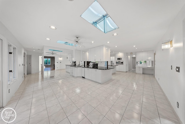 kitchen featuring white cabinetry, ceiling fan, a skylight, and light tile patterned floors