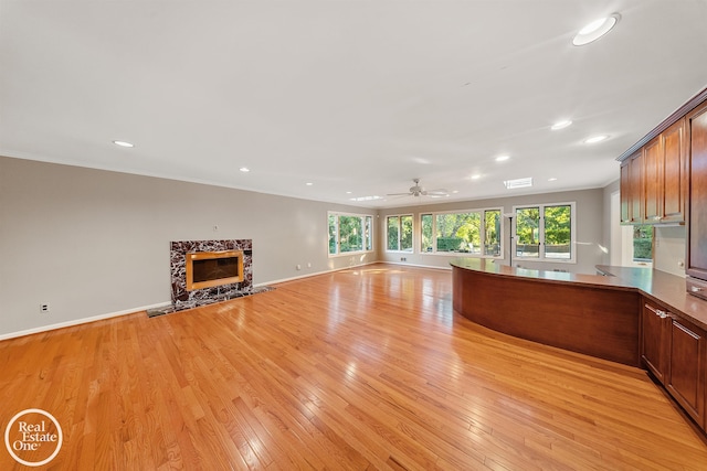 unfurnished living room with a ceiling fan, crown molding, light wood-style floors, a premium fireplace, and recessed lighting