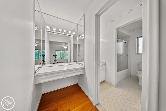 bathroom featuring toilet, vanity, baseboards, bath / shower combo with glass door, and ceiling fan