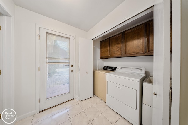 clothes washing area with washing machine and dryer, light tile patterned floors, and cabinets