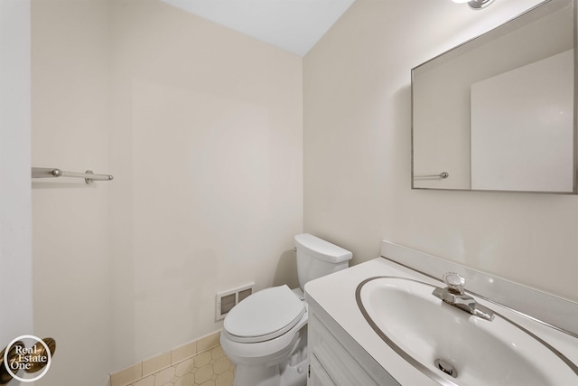 half bath with toilet, vanity, visible vents, and baseboards