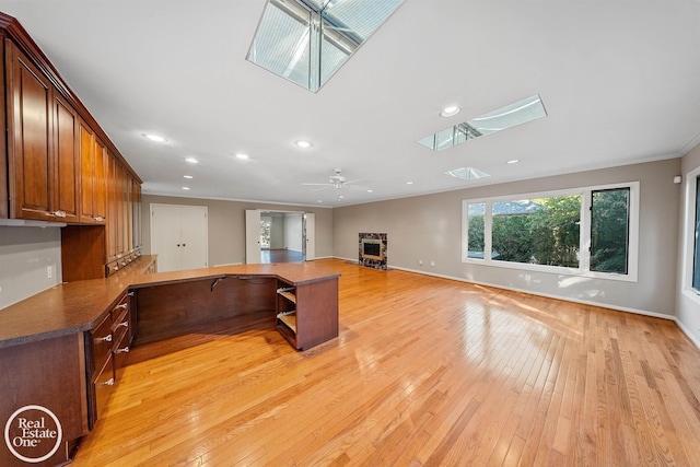 kitchen featuring ceiling fan, crown molding, a skylight, and light wood-type flooring