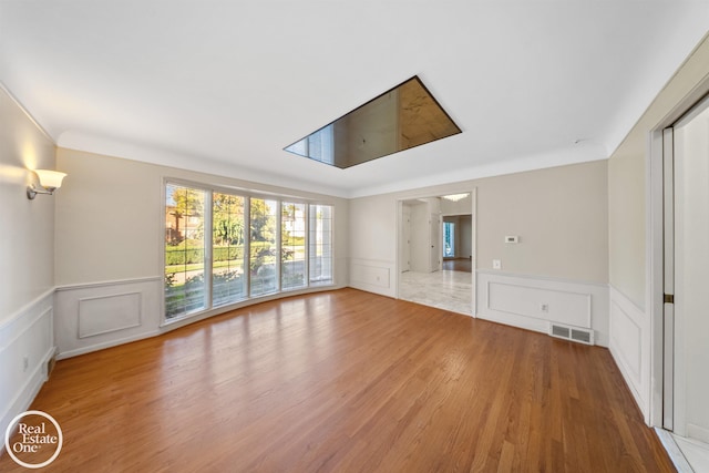 unfurnished living room featuring wainscoting, light wood-style flooring, visible vents, and a decorative wall