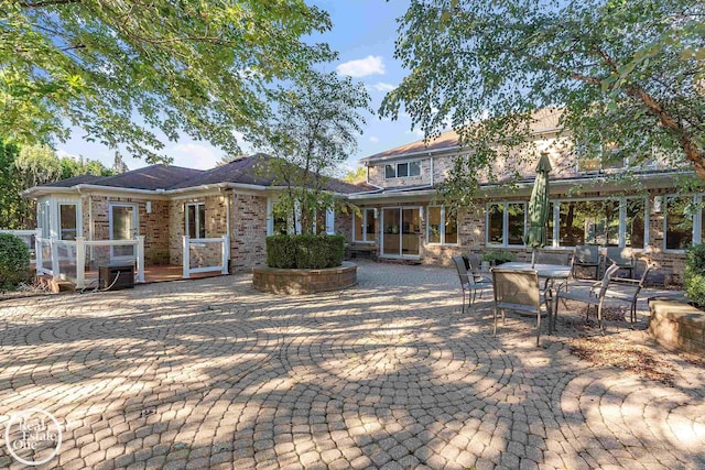 back of property featuring brick siding, a wooden deck, and a patio