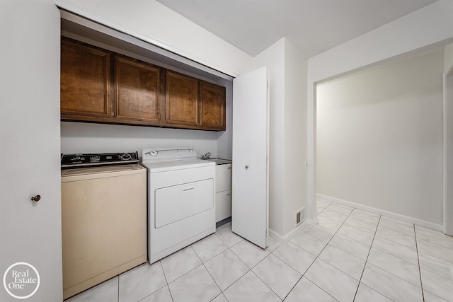 clothes washing area with independent washer and dryer, light tile patterned flooring, and cabinets