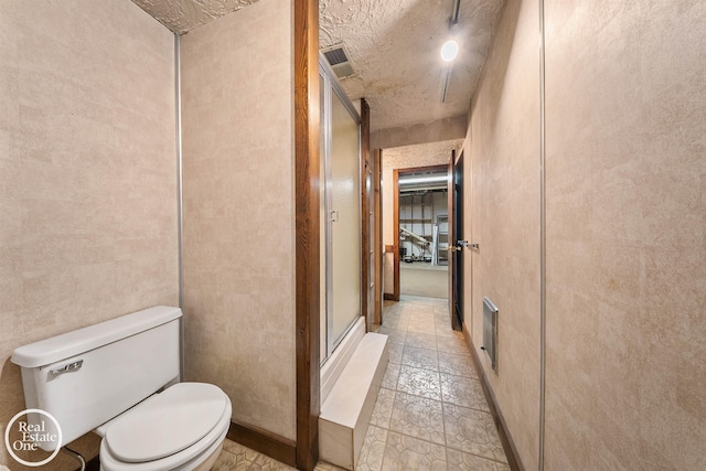 bathroom with toilet, a textured ceiling, a stall shower, baseboards, and visible vents