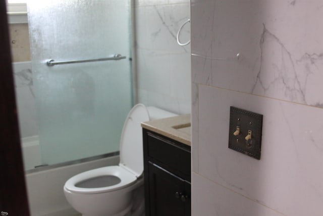 full bathroom featuring vanity, toilet, tile walls, and combined bath / shower with glass door