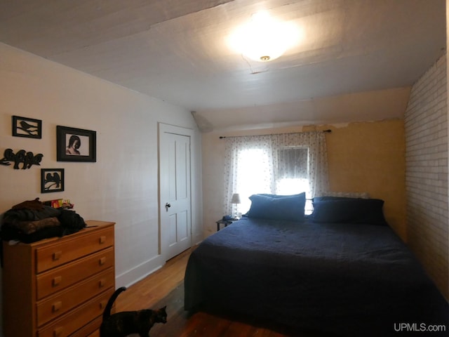 bedroom featuring brick wall, vaulted ceiling, wood-type flooring, and a closet