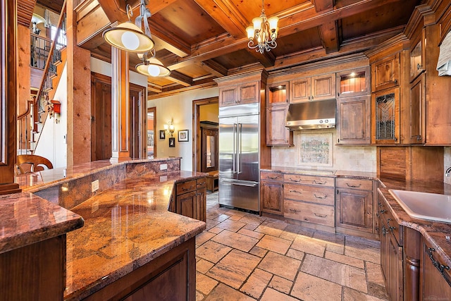 kitchen with hanging light fixtures, backsplash, dark stone countertops, built in fridge, and sink