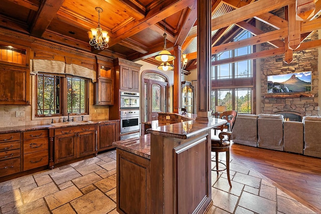 kitchen featuring sink, a kitchen bar, hanging light fixtures, beamed ceiling, and dark stone counters