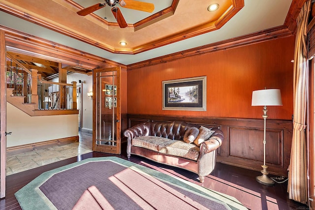 living area with crown molding, a raised ceiling, and ceiling fan