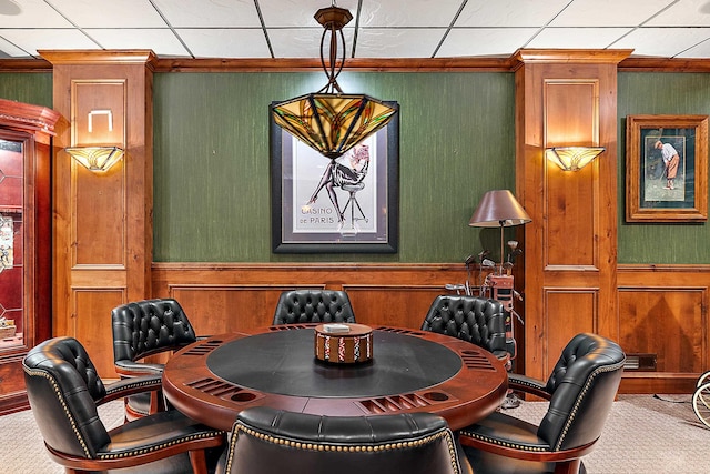 carpeted dining room featuring a drop ceiling and wood walls