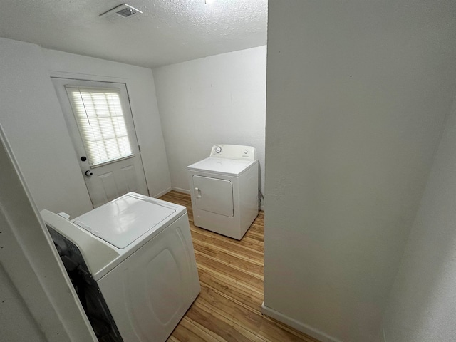 clothes washing area featuring light hardwood / wood-style flooring, washer and dryer, and a textured ceiling