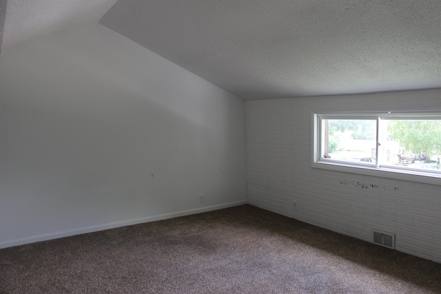 carpeted spare room featuring brick wall, a textured ceiling, and lofted ceiling