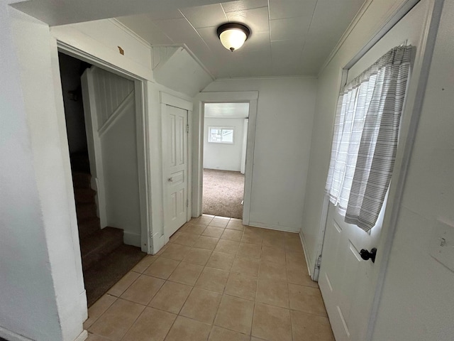 hall with ornamental molding, lofted ceiling, light tile patterned flooring, and a healthy amount of sunlight