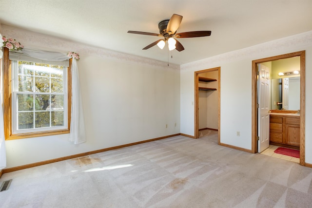 unfurnished bedroom with a closet, a walk in closet, light colored carpet, ensuite bathroom, and ceiling fan