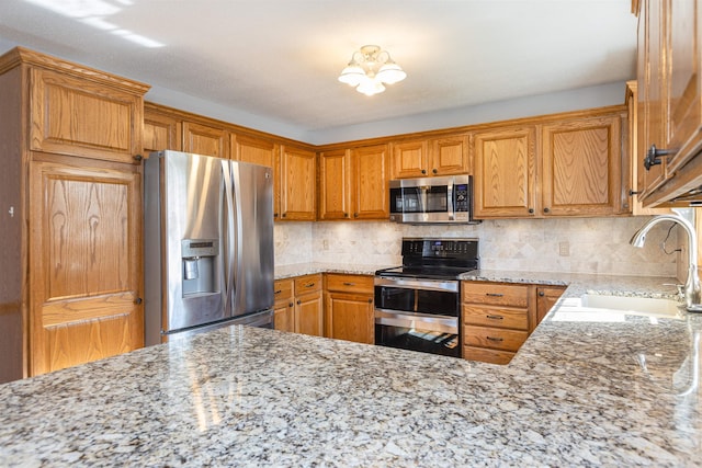 kitchen with light stone counters, stainless steel appliances, sink, and backsplash