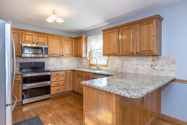 kitchen featuring kitchen peninsula, backsplash, sink, light wood-type flooring, and appliances with stainless steel finishes