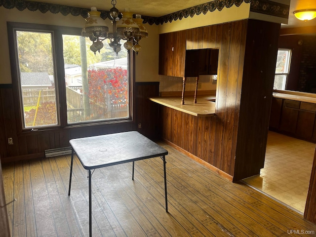 unfurnished dining area featuring a baseboard heating unit, a chandelier, light wood-type flooring, and wooden walls