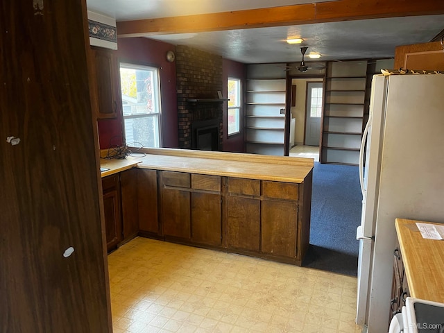 kitchen with kitchen peninsula, wooden counters, a brick fireplace, and white refrigerator