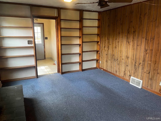 interior space with ceiling fan, wood walls, and carpet flooring