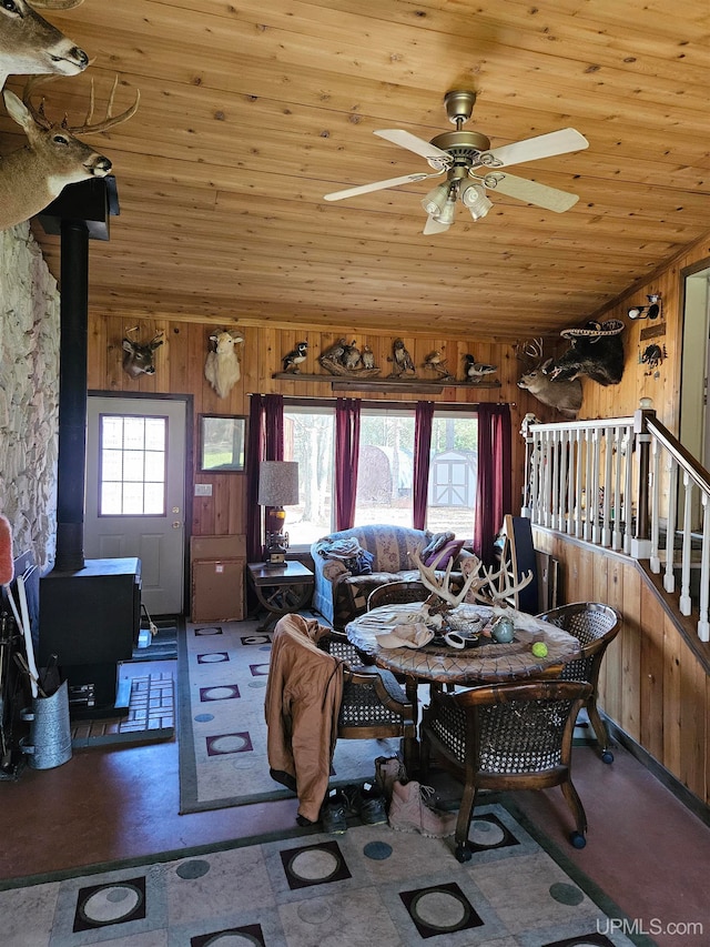 dining room featuring a wood stove, a healthy amount of sunlight, and wooden walls