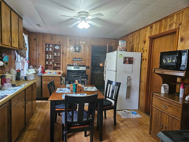 dining room with light wood finished floors, ceiling fan, visible vents, and wood walls