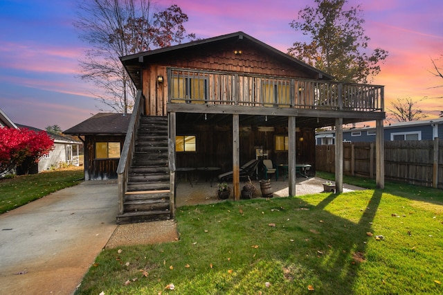 back house at dusk with a yard, a deck, and a patio