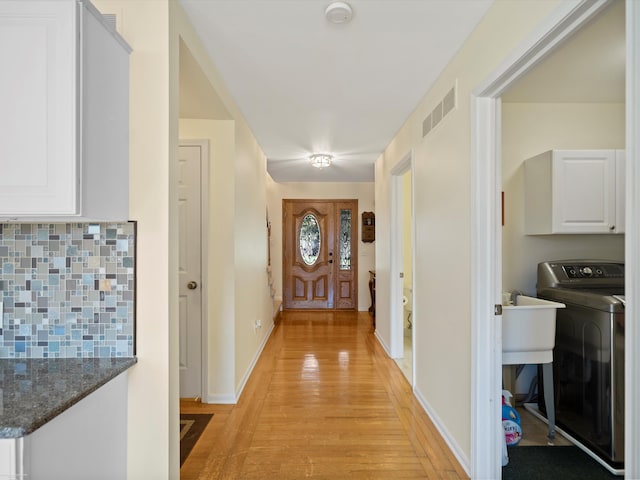 corridor featuring baseboards, light wood-style flooring, washer / clothes dryer, and visible vents