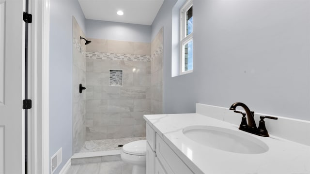 bathroom with a tile shower, vanity, and toilet