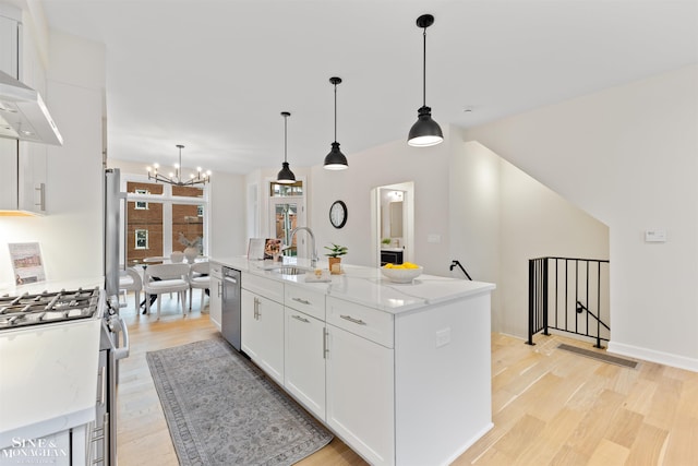 kitchen with a kitchen island with sink, hanging light fixtures, stainless steel appliances, white cabinetry, and light hardwood / wood-style floors