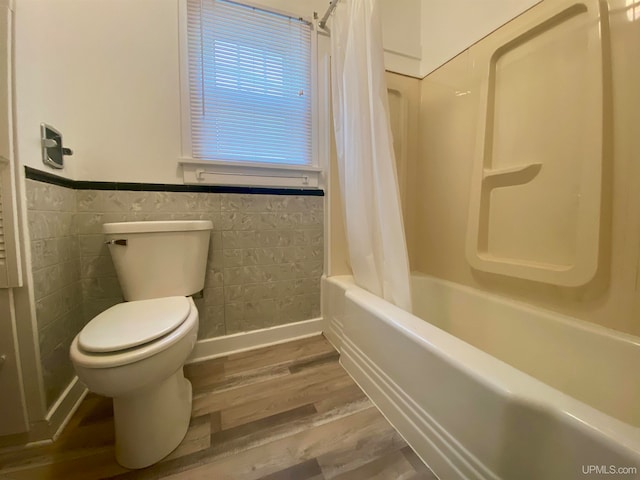 bathroom with toilet, hardwood / wood-style flooring, tile walls, and shower / tub combo